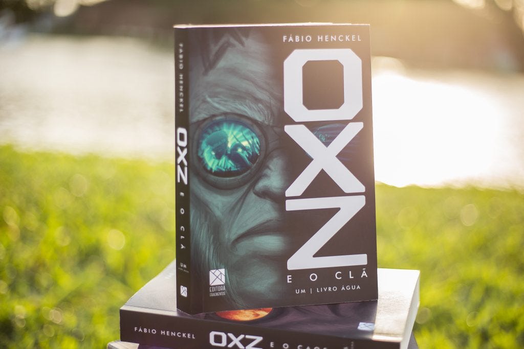 Livro O.X.Z e o Clã, em uma praça. Ao sol.