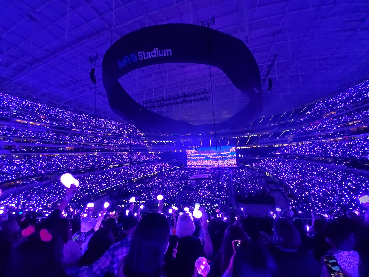 A deep purple light over a stadium full of people holding light sticks.