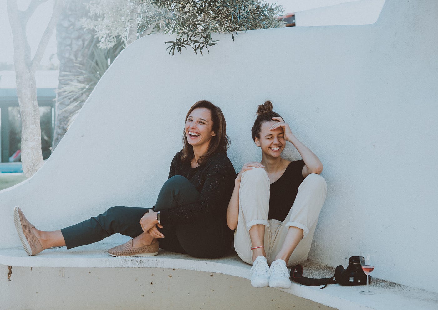 Two laughing women sitting on a concrete ledge