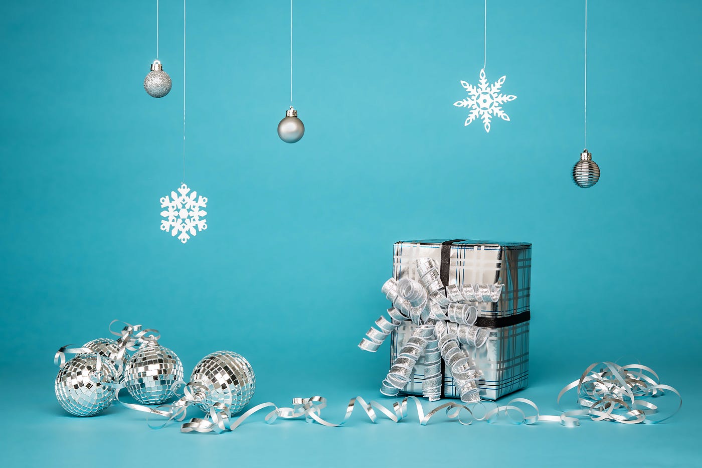 Silver wrapper Christmas present surrounded by silver Christmas ornaments on blue background