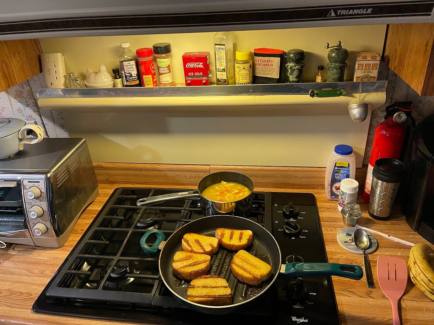 Soup simmering on an electric stove along with garlic bread heating in a pan.