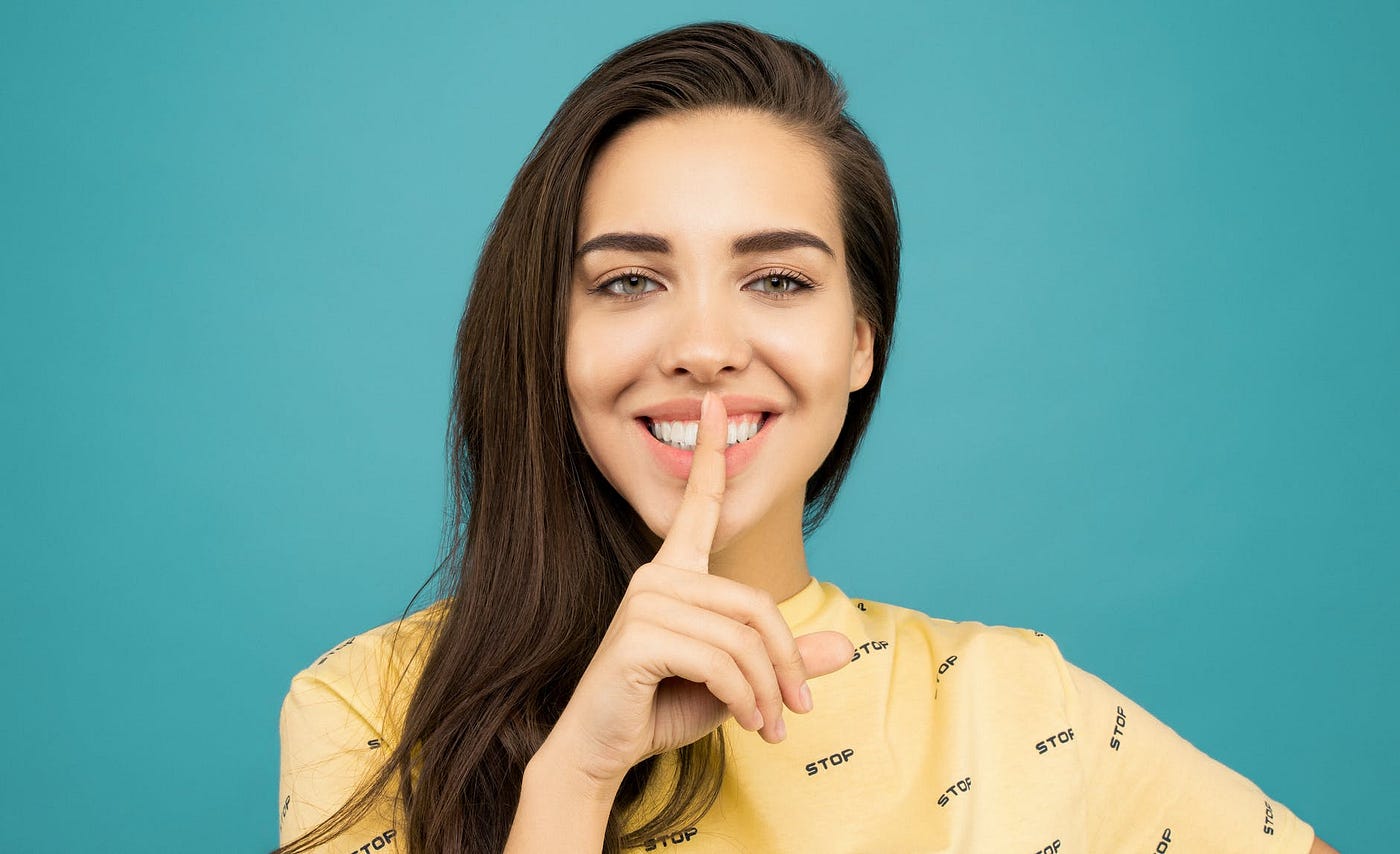 Photo of woman wearing a yellow shirt and asking an audience to keep a secret
