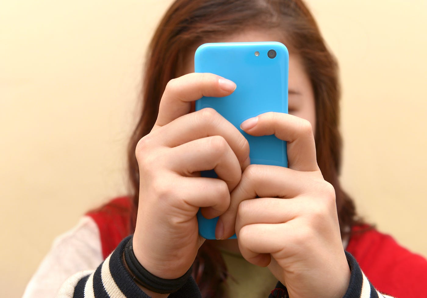 Close up of a teenager using her smartphone. Her face is obscured by her phone.