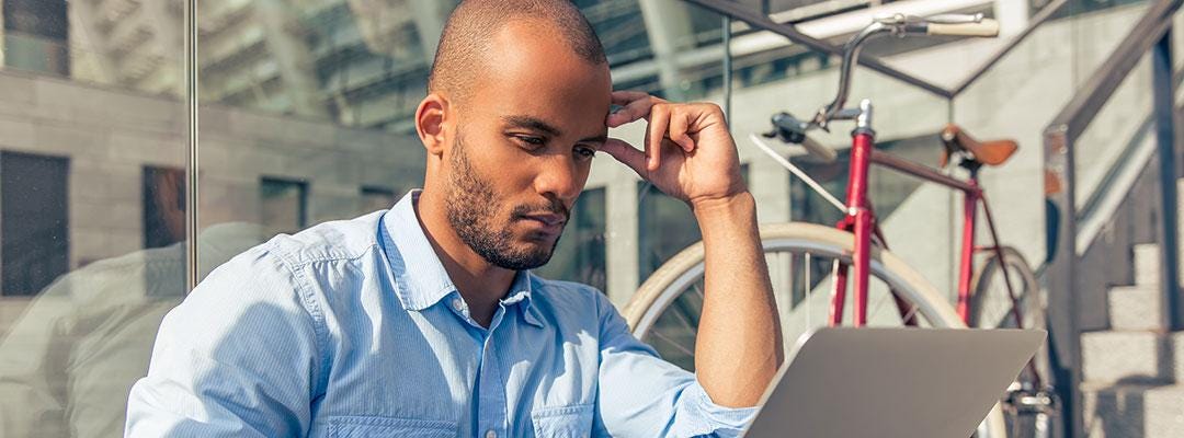 Black male professional wearing a blue-collar shirt working on a laptop