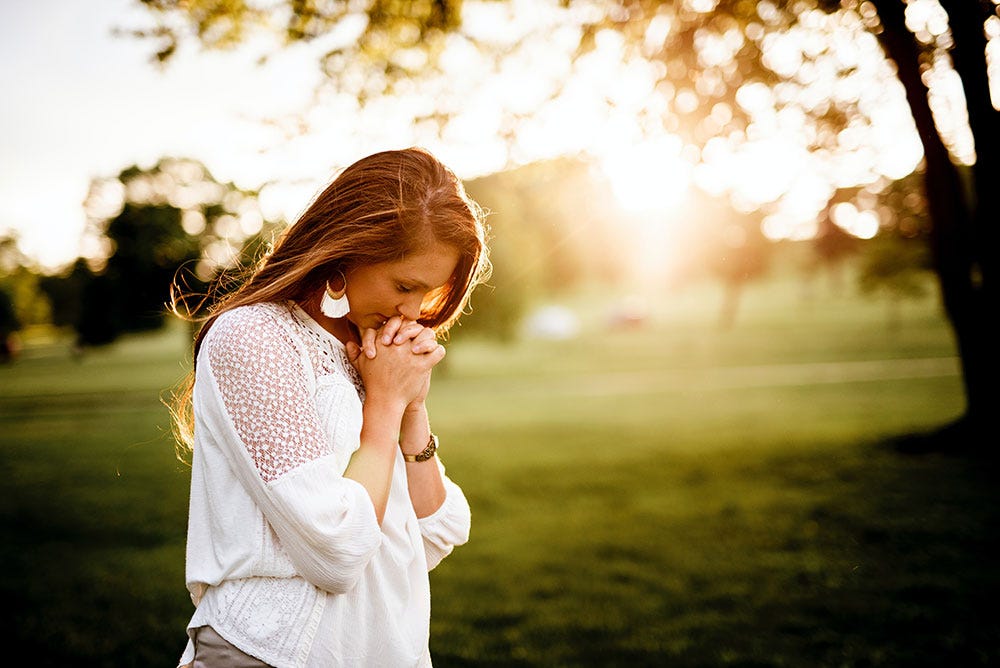 Woman in park deep in thought, hands clasped together.