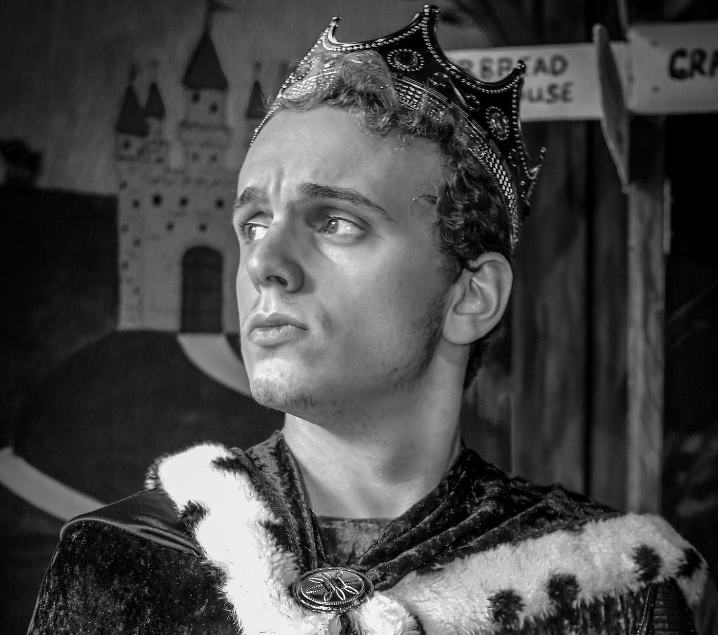 A young man in a crown and ermine robe glances sideways, seemingly bored.