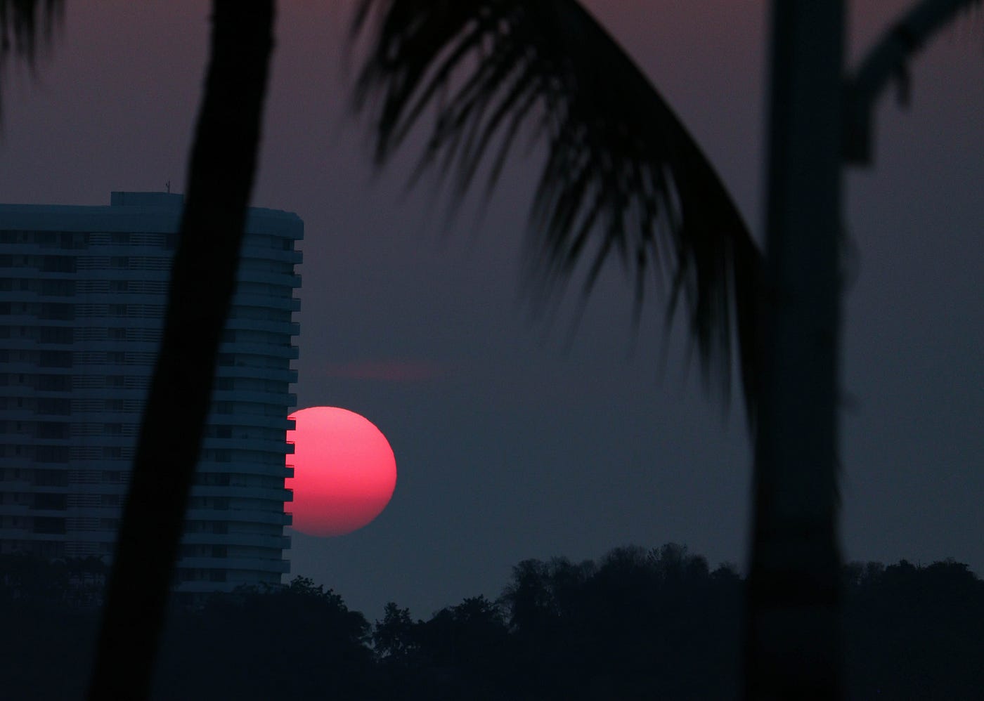 The pink moon rising partially obscured by a building