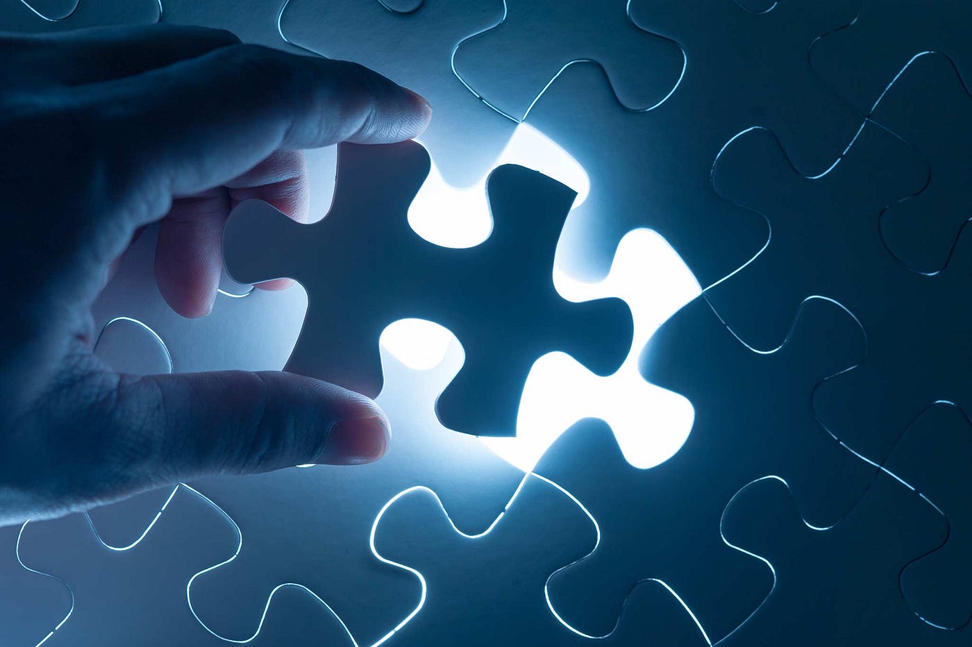 A hand holds the final piece of a puzzle over it’s opening, which emits a bright, white light.