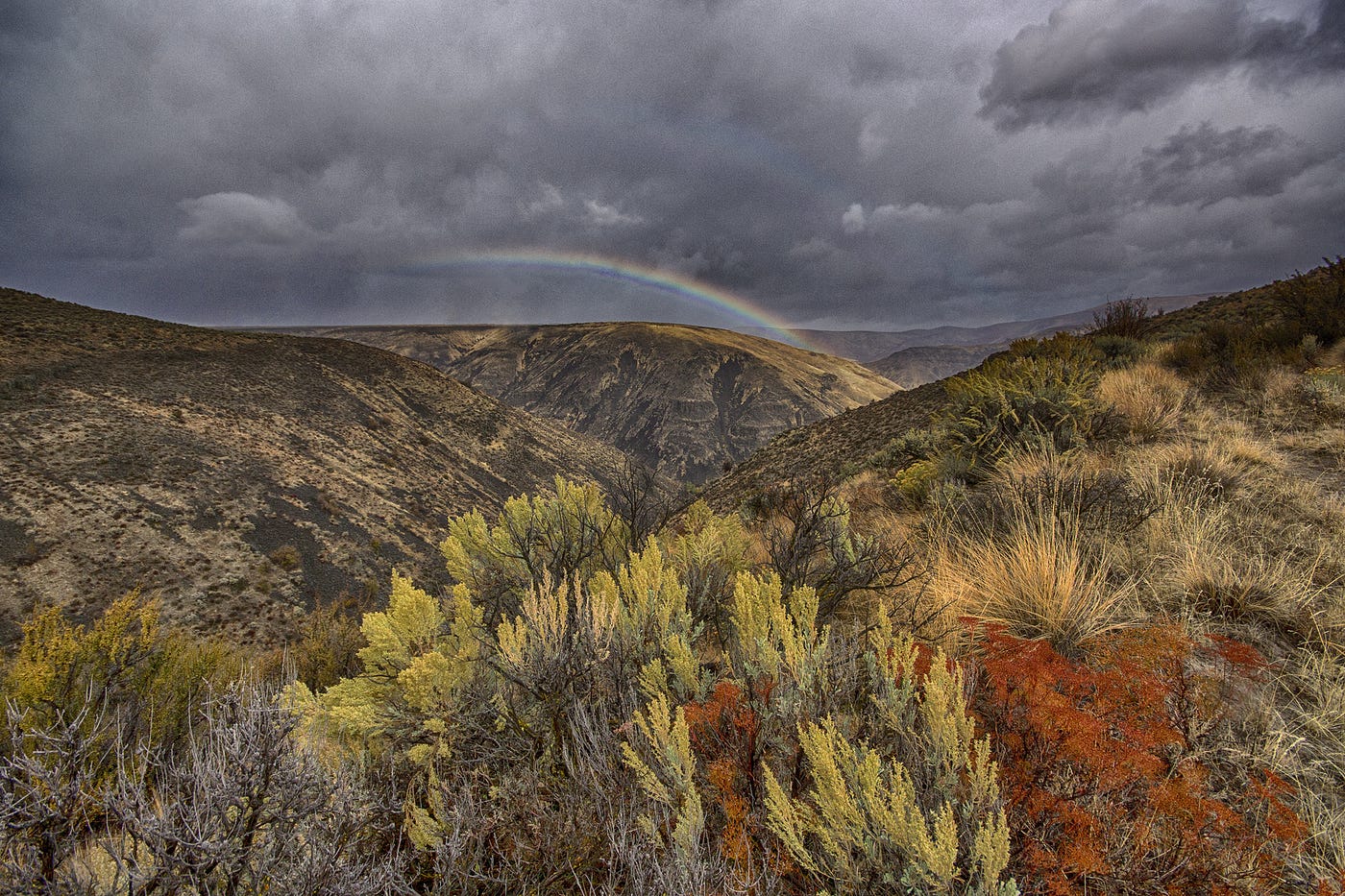 A rainbow arches over hillsides under gloomy skies in the Wenas Wildlife Area in Eastern Washington.