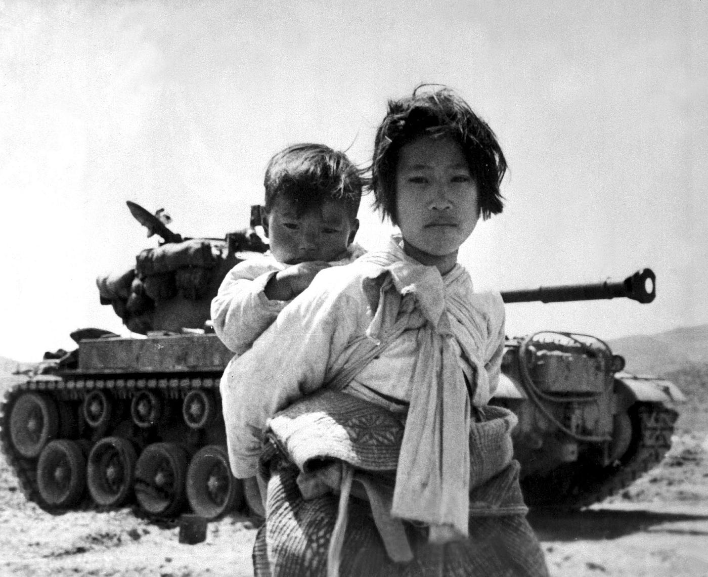 An archival photo from the Korean War. Carrying her baby brother on her back, a war weary Korean girl walks by a stalled M-26 tank, at Haengju, Korea, June, 1951.