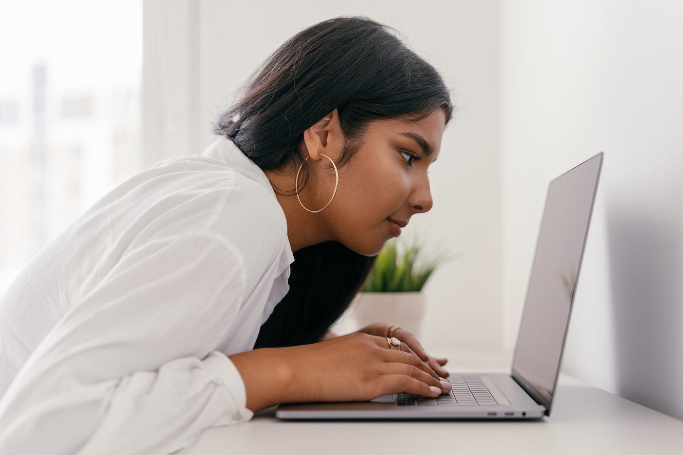 woman in white shirt staring closely at computer screen