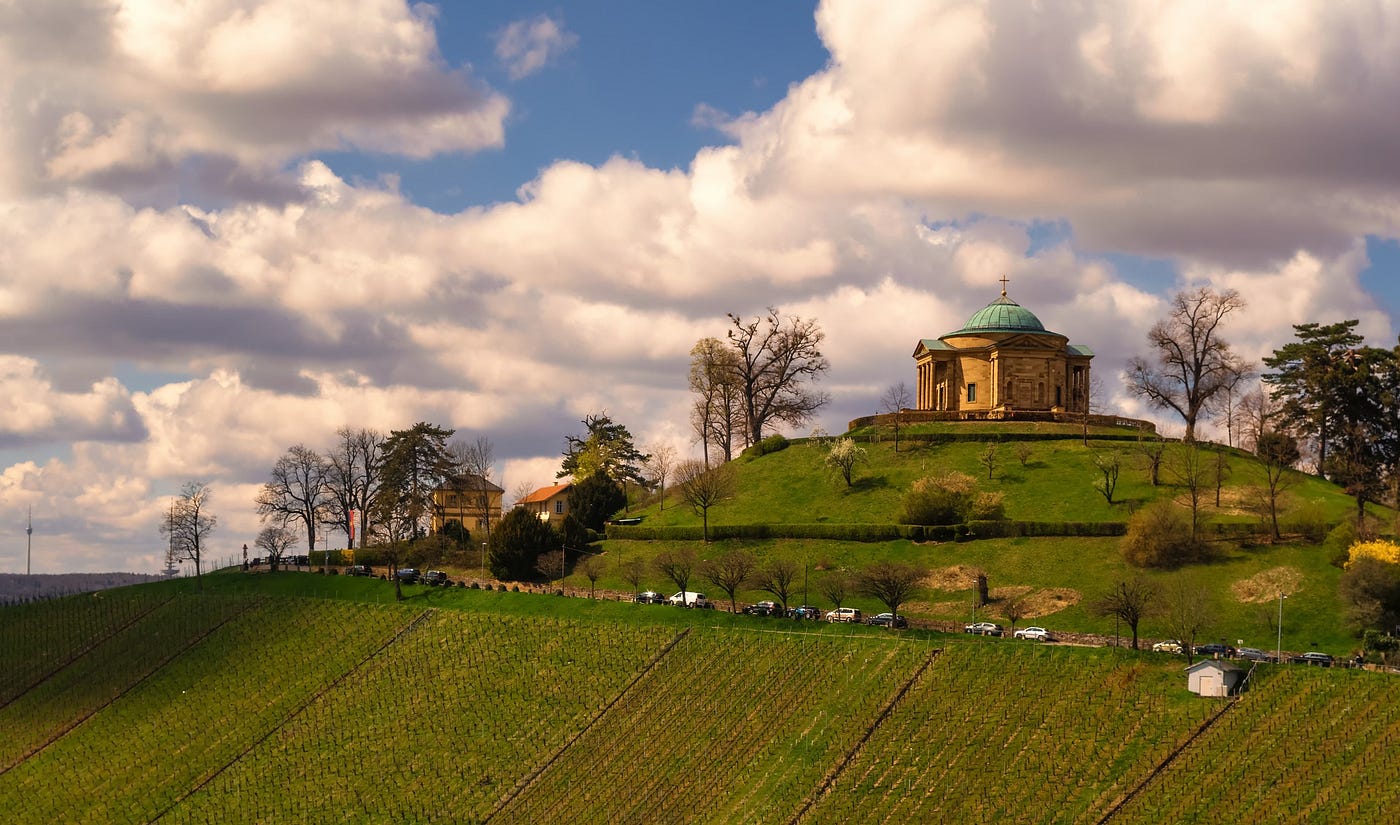 A grand sandstone Church set in a rural green hillside with vaguely surreal clouds in Rotenberg, Stuttgart, Germany