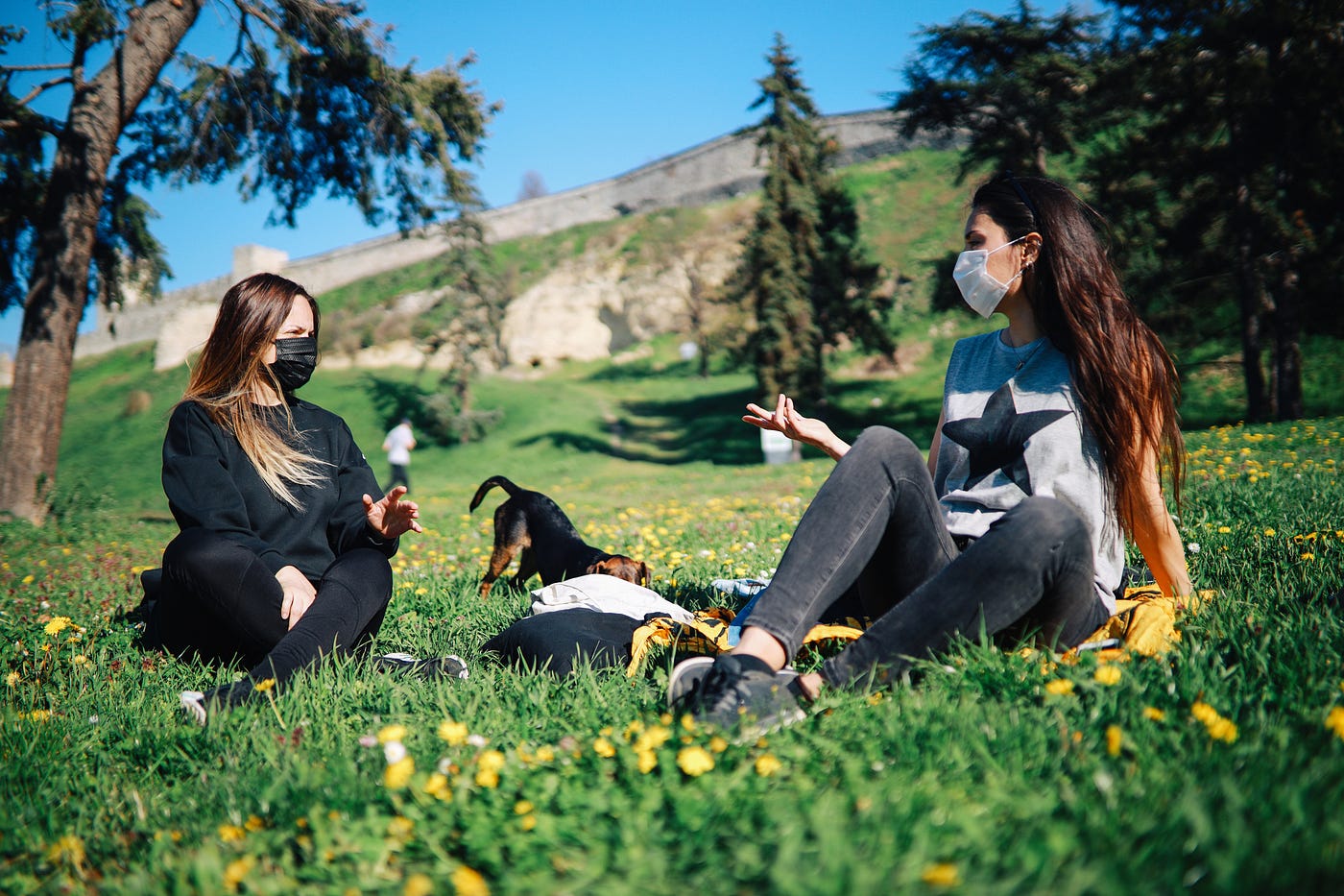 Two young women with protective masks hanging out in the park with a dog during the coronavirus outbreak.