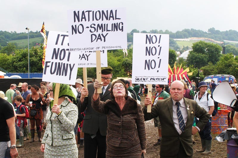 Picture of several people holding different signs. One says National No-smiling day. Another simply says NO! NO! NO! These “protesters” appear to be from the British Pessimists League.
