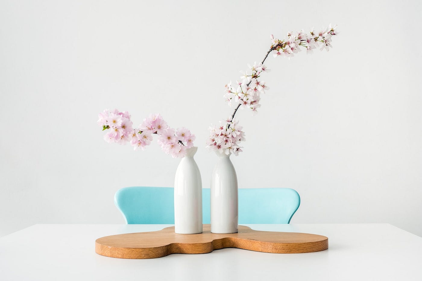 Two white vases with a stalk of flower each kept on a wooden board