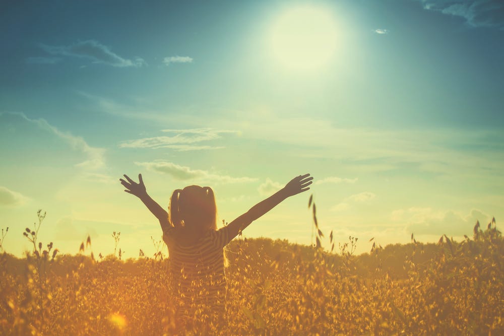 Person standing in the sunshine with hands up in happiness.