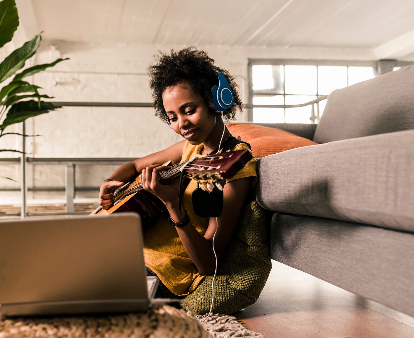 A Black woman learning to play the guitar from an online video.