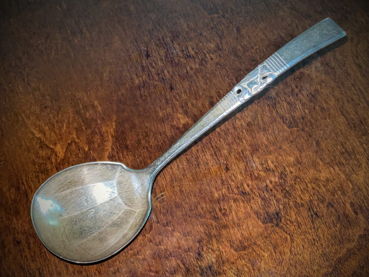 Large tarnished and scratched silver gravy ladle against a wood background.