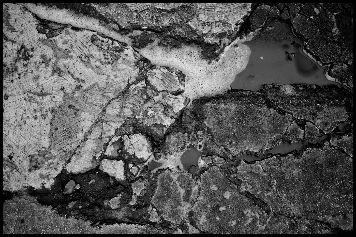 Close up view of a water puddle with foam in a cracked and broken sidewalk.