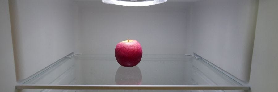 One red apple on an otherwise empty fridge shelf. Variety: Pink Lady.