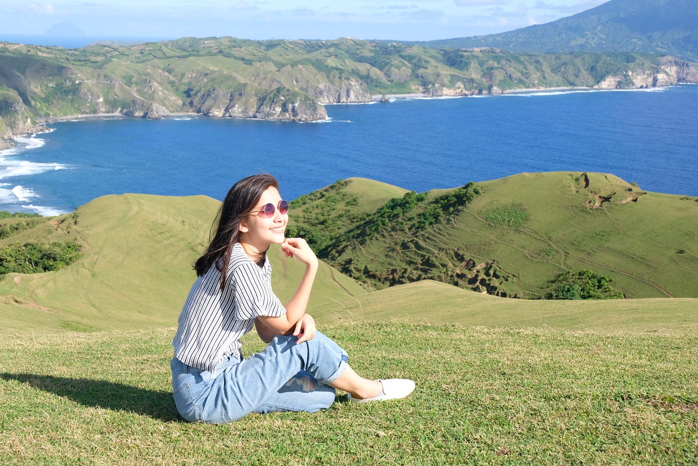 A smiling girl sitting on top of a sun-lit hill