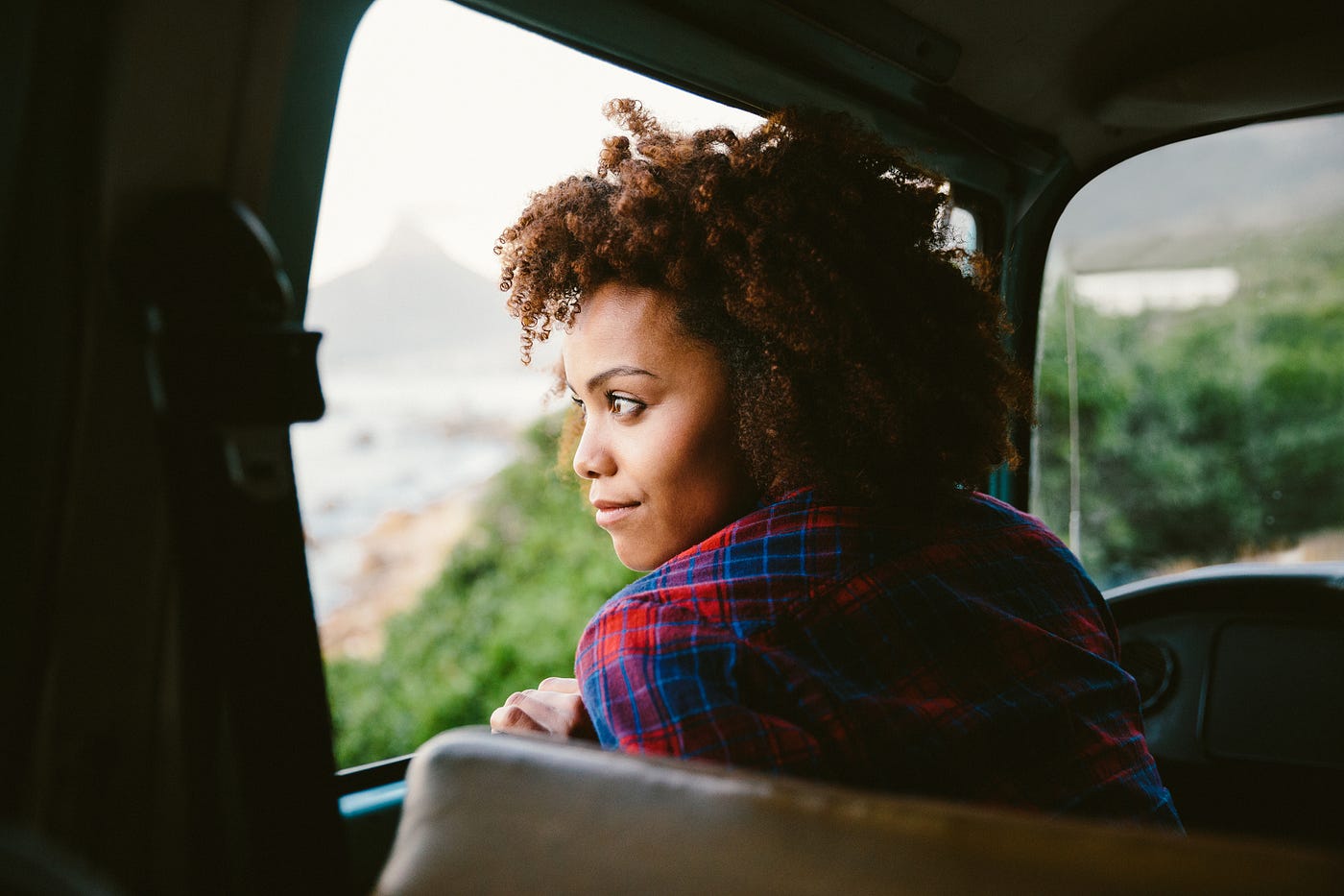 Black woman looking out the window of her car from the driver seat.