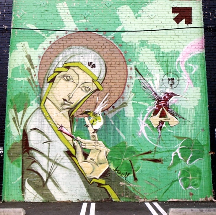 Mural on a brick wall of a smiling Madonna with a hummingbird perched on her finger