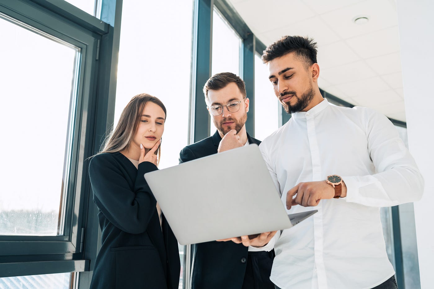 Three business people standing and reading a report on a laptop