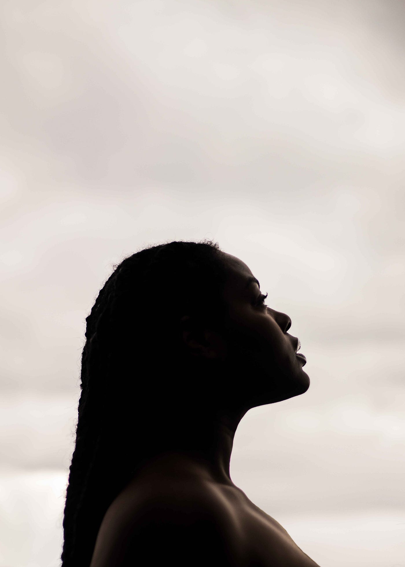 A Black woman looks up pensively in a white background.