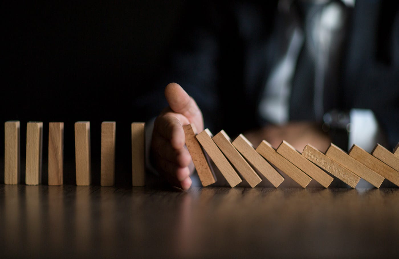 A hand in between a row of falling dominoes to stop them from knocking over the rest.