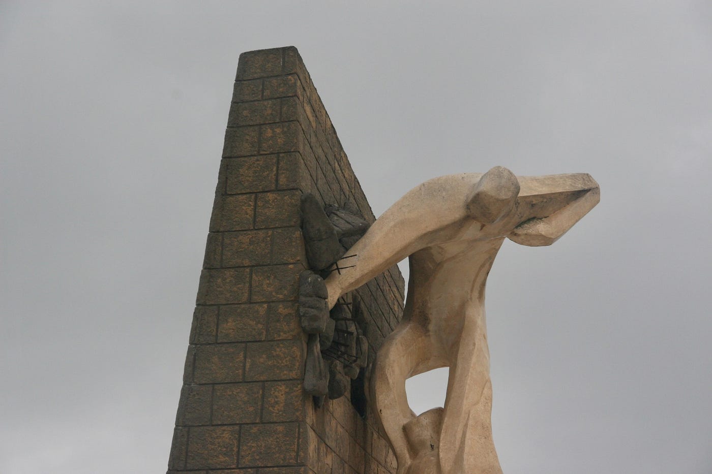 Color photo of a statue of a man in active life struggle on the side of a wall.