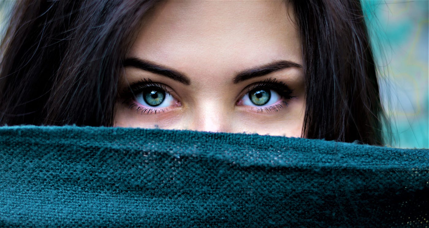 close-up of woman’s face with piece of fabric covering from the nose down brown hair green eyes