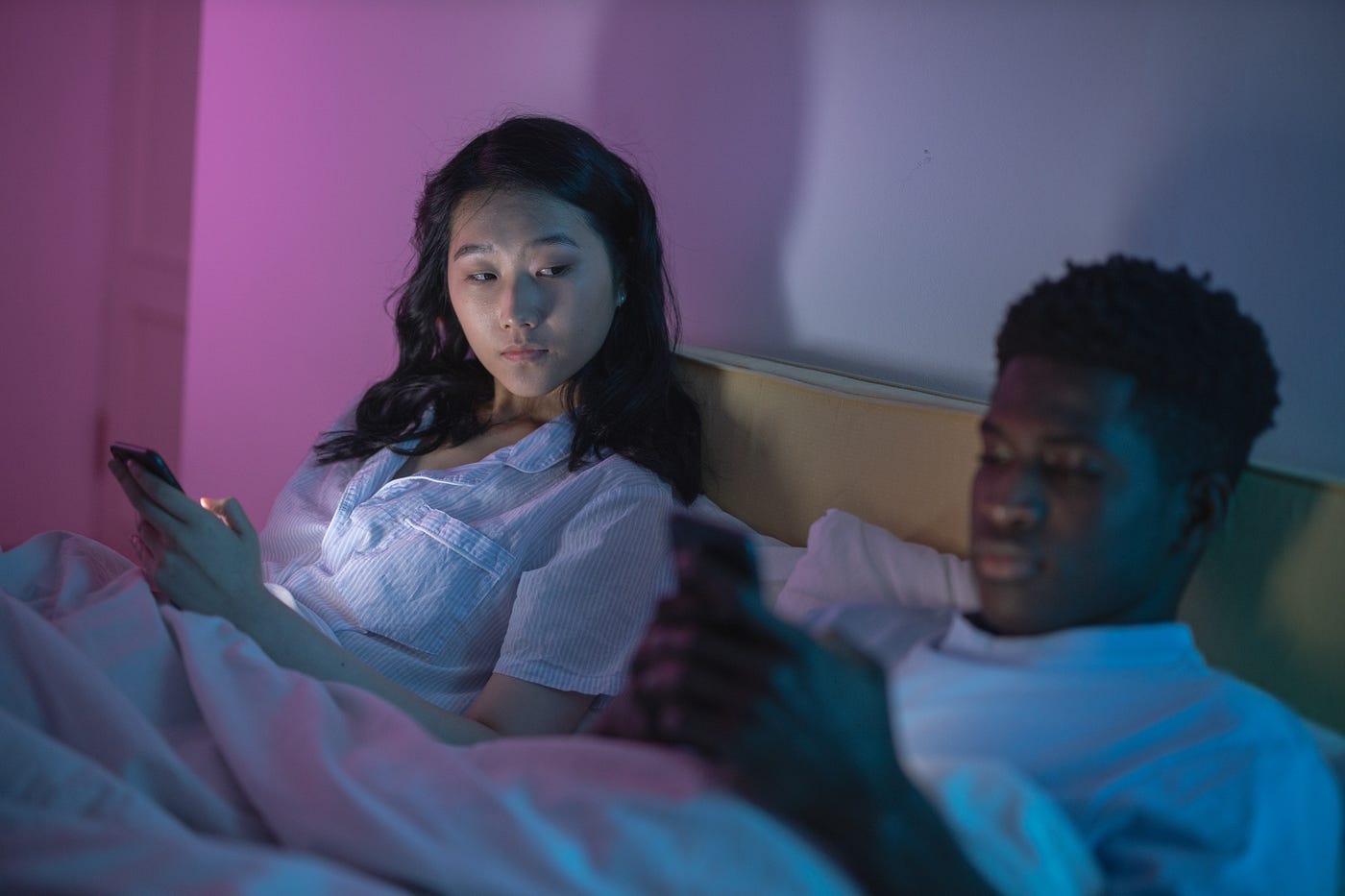 Asian woman looking at her black boyfriend on the bed who is looking at his phone