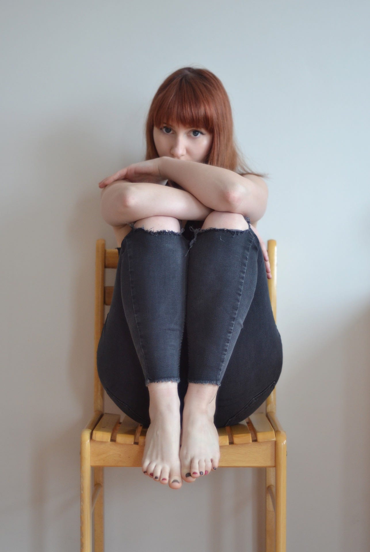 young teenager with red hair, sitting in chair, hugging her knees and just peeking out with her eyes Lisa Gerard Braun Medium