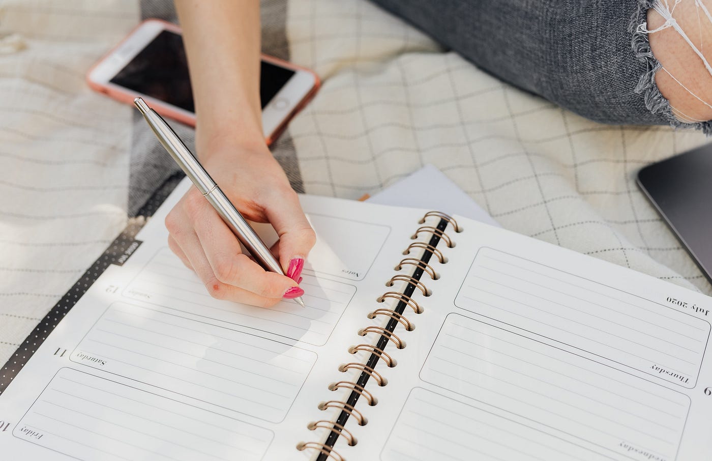 Cropped woman sitting on blanket taking notes in a weekly planner. Create an ideal week template.