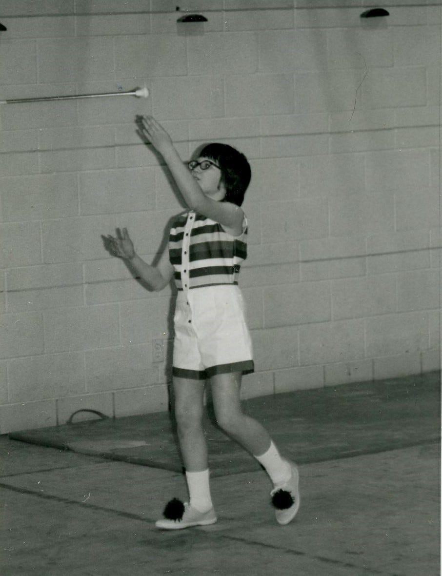 Black and white image from the mid 70’s of a girl in shorts and sleeveless top tossing a baton in the air