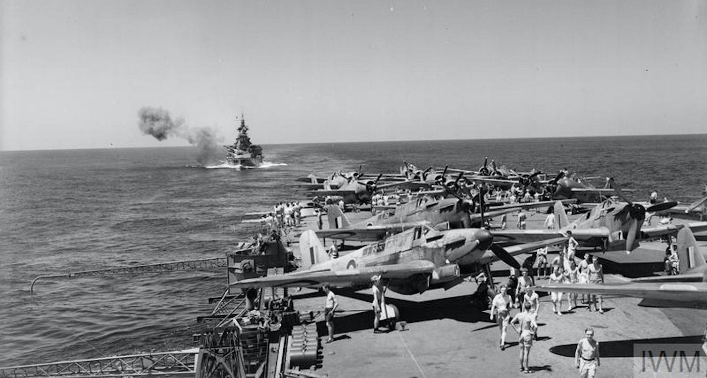 HMS Valiant in the background during a practice shoot on exercise. Fairey Fulmars (planes) in the foreground onboard Aircraft Carrier HMS Illustrious. © IWM A 15153