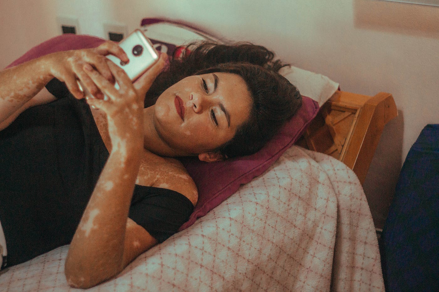 A photo of a young woman lying in bed, texting on her phone.