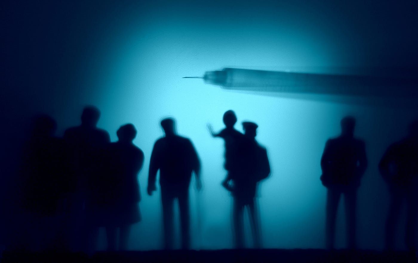 The silhouette of a vaccine shot hovering over dark silhouettes of people from various age groups.