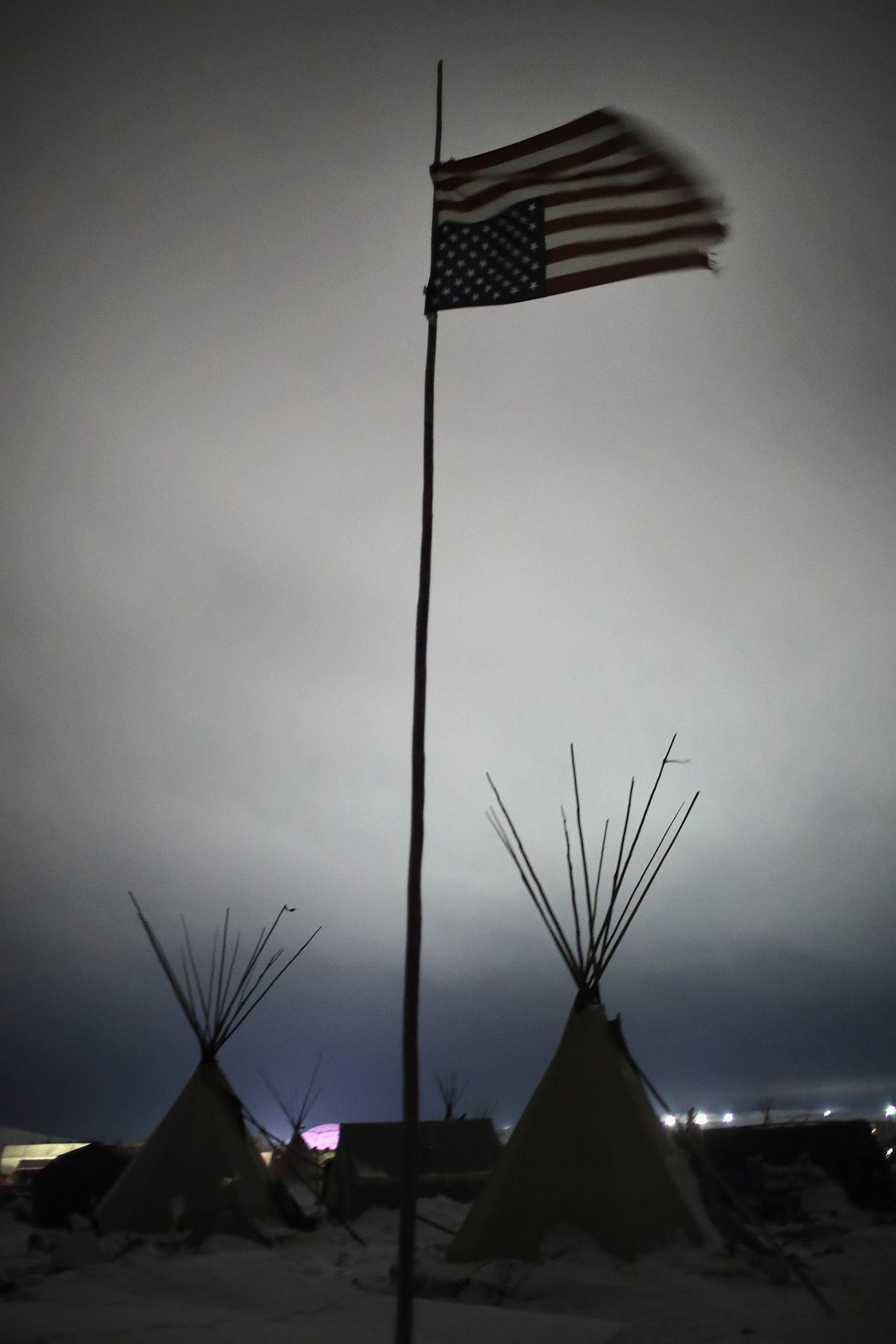 A photo of an upside down American flag hanging over a dark, ominous sky in Oceti Sakowin Camp.