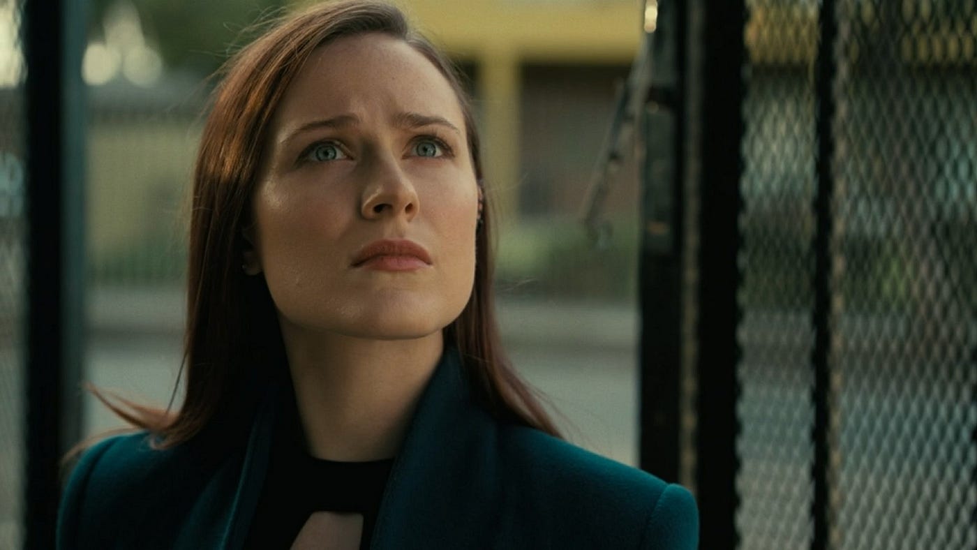 Evan Rachel Wood as Christina in Westworld Season 4, with reddish hair, blue eyes, and light red lipstick. She’s wearing a dark green velvet jacket and is staring up at something out of the frame, looking concerned.