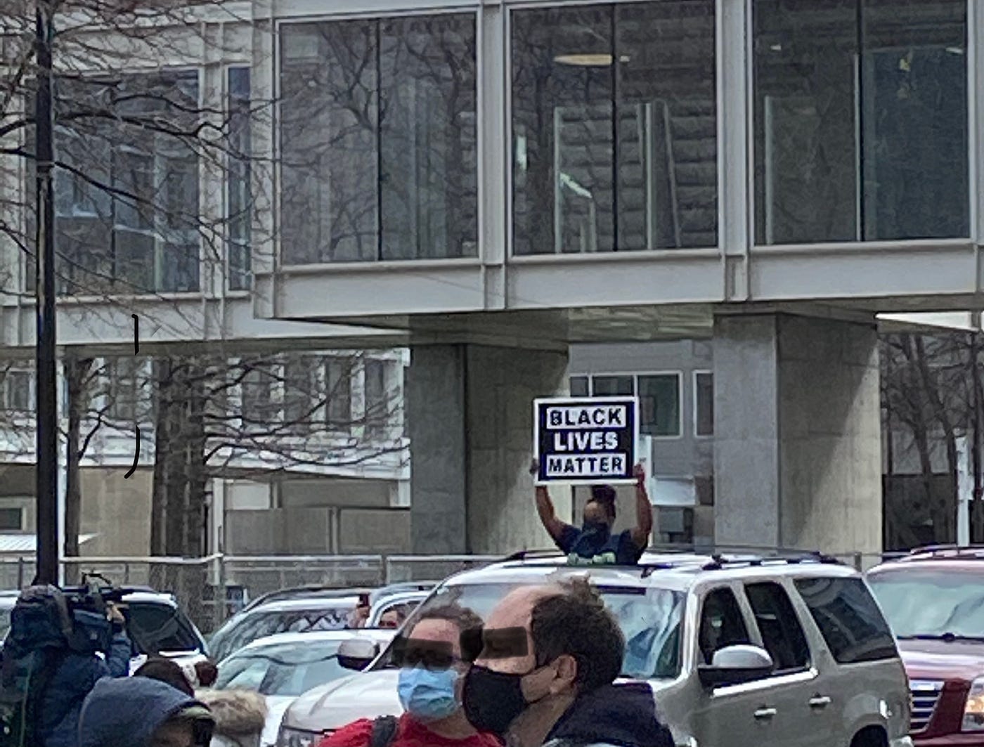 Young woman holding up a “Black Lives Matter” sign out of a car sun roof in front of a crowd of people