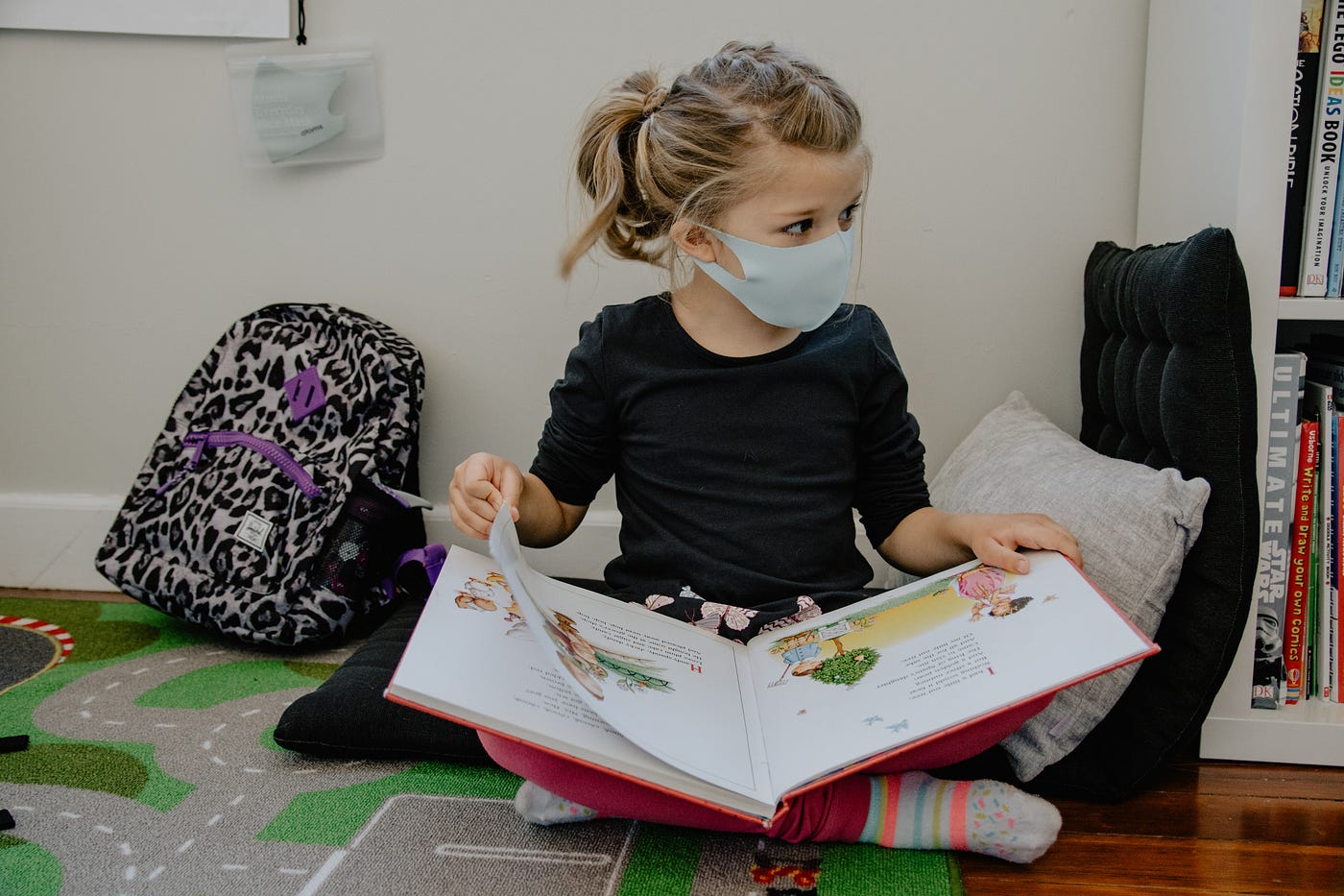 girl with mask on and backpack reading a book