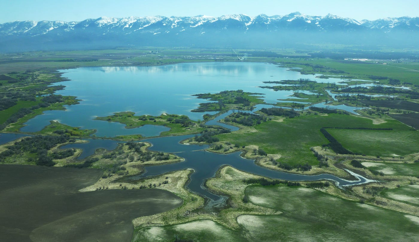A reservoir surrounded by lakes, wetlands, and grasslands backdropped by snow-capped mountains