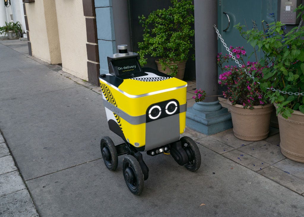 A photo of a Postmates food delivery robot going down a sidewalk.