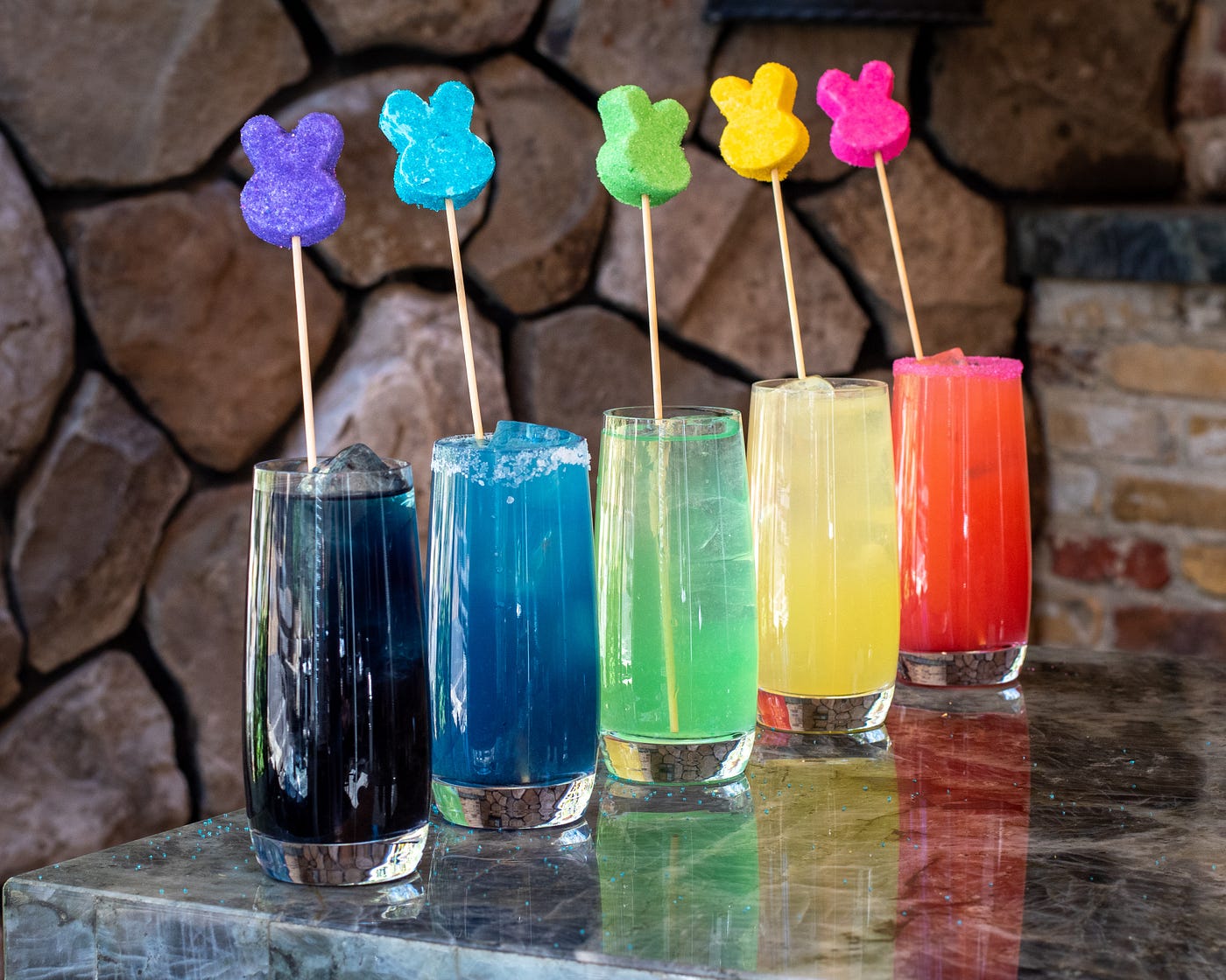 Five different colored easter peeps sticking out of a the same colored drink in a row.