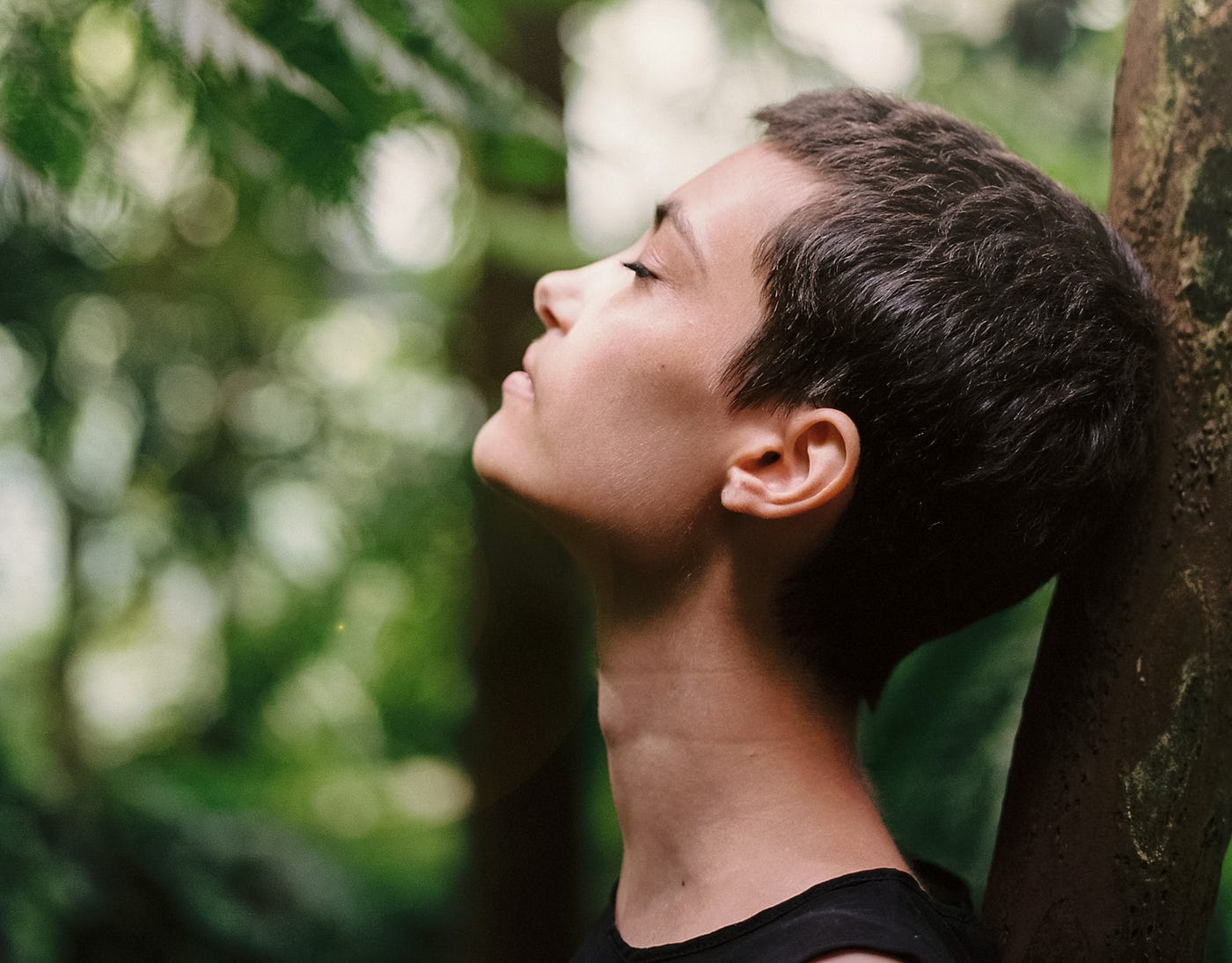 A person leans back against a tree with their eyes closed.