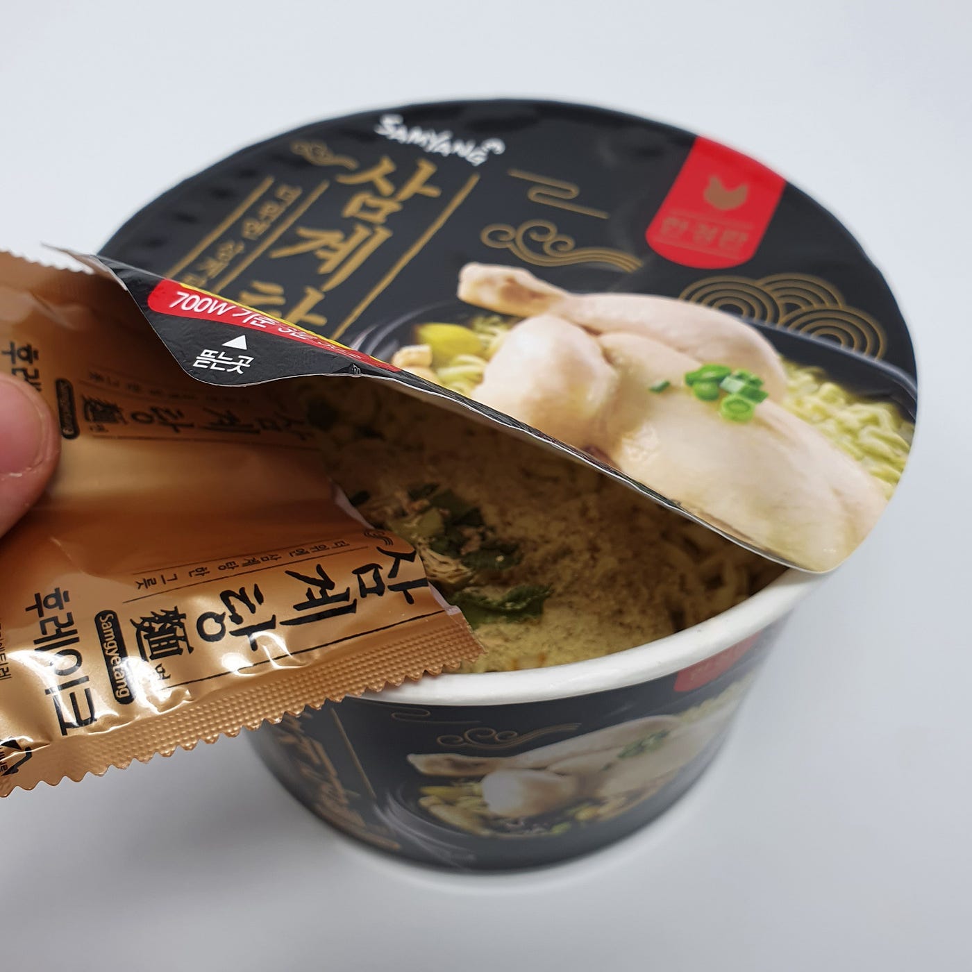 Adding the dried flakes packet into a cup of Samyang Samgyetang Myeon Instant Noodles.