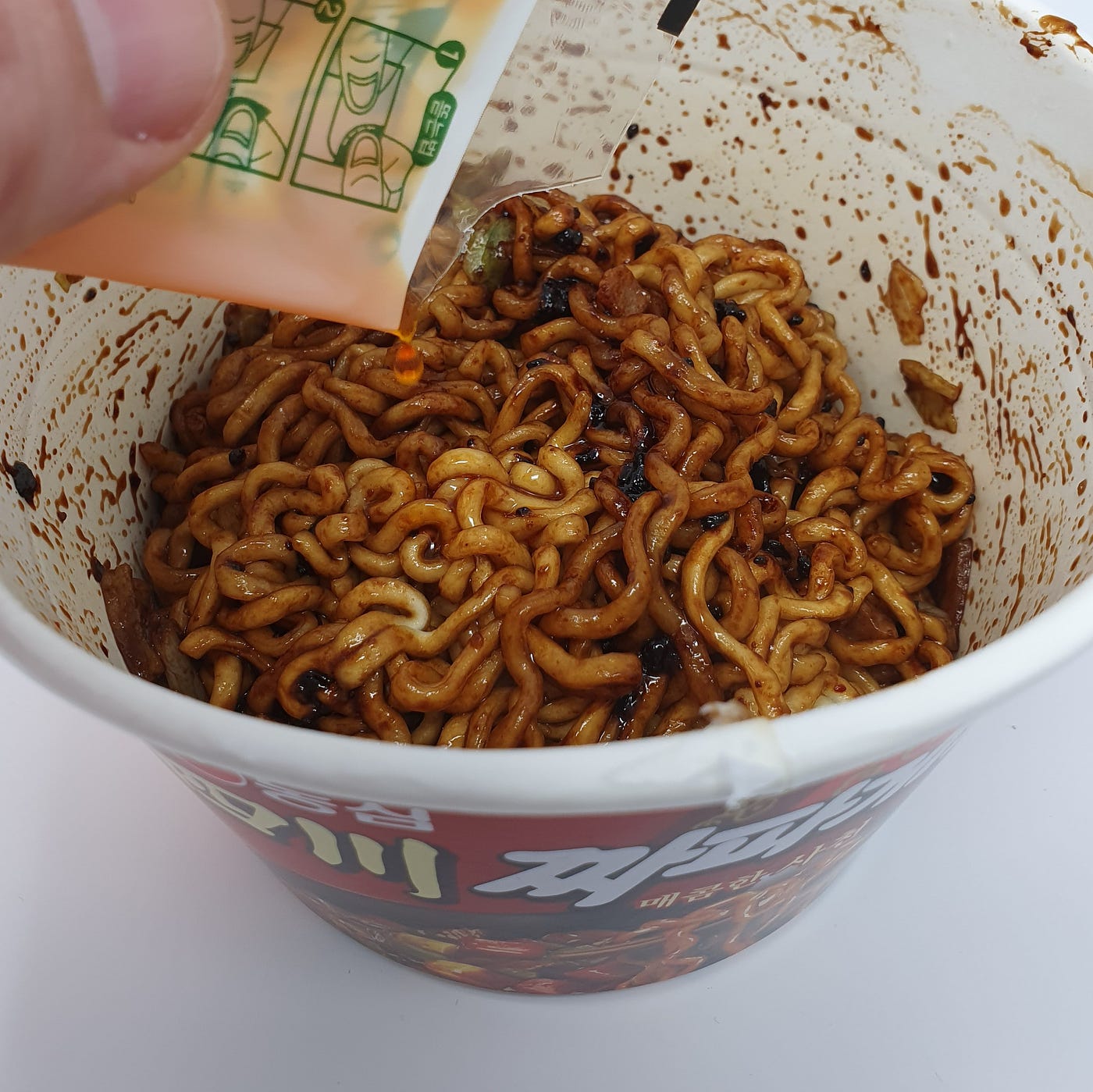 Adding the flavored pepper oil to a cup of Nongshim Sacheon Chapagetti Instant Noodles.