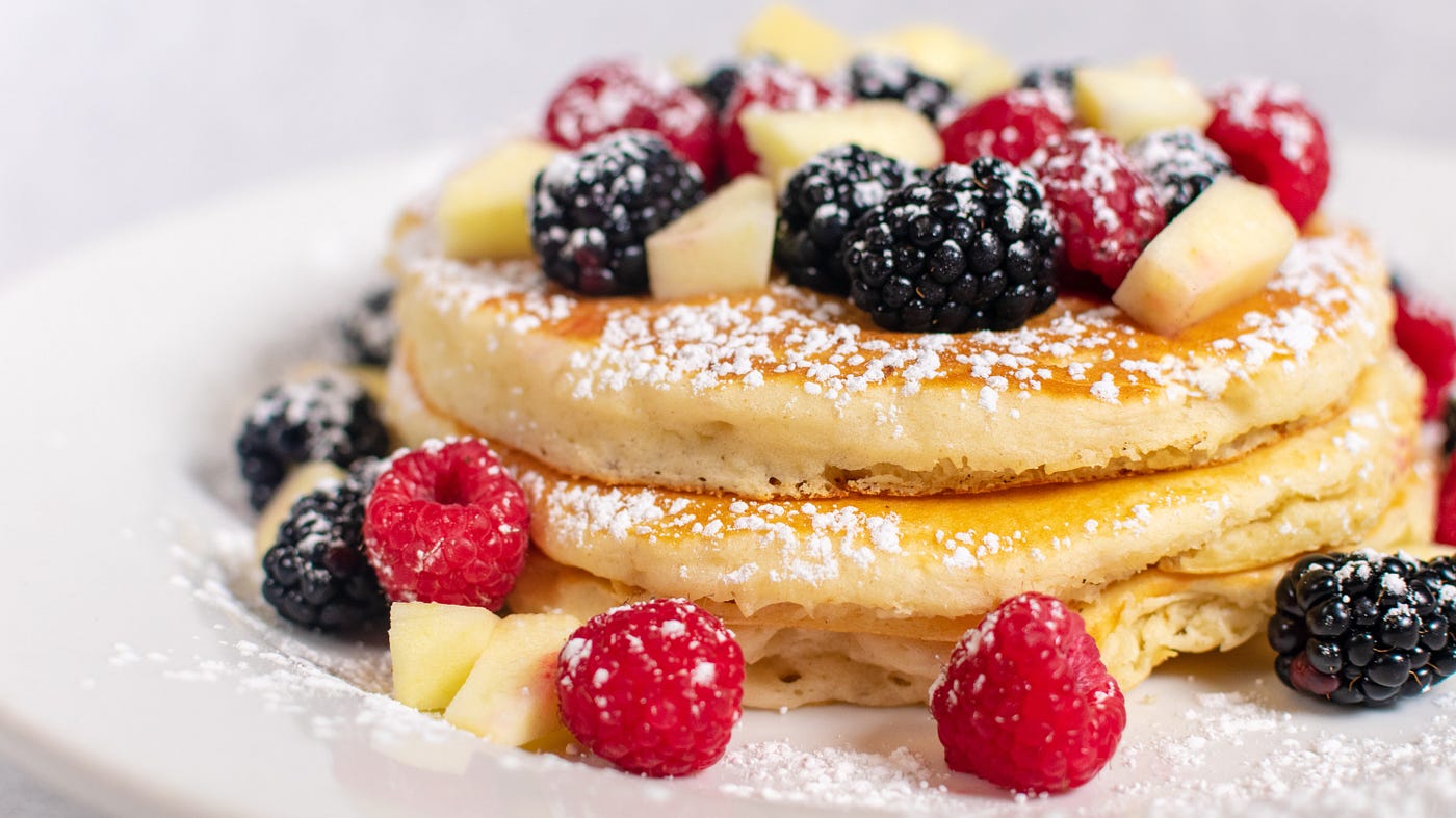 Up close of pancakes with fresh fruit and a sprikle of powderd suger.